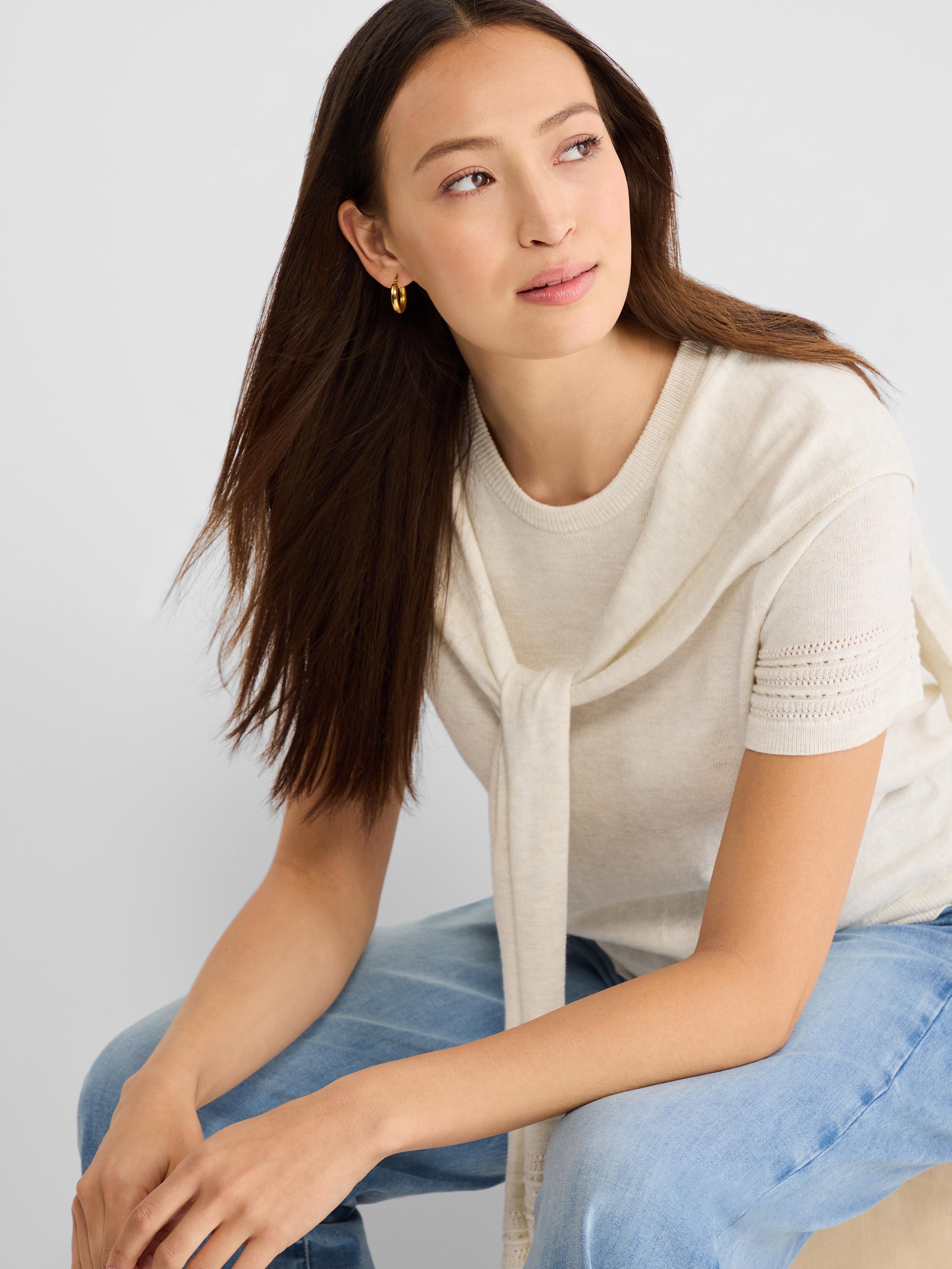 Cream short-sleeve knit top with eyelet cuff detail, styled with a matching sweater tied draped over the neck.