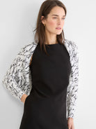 White knit shrug cardigan with black cursive pattern, worn open.