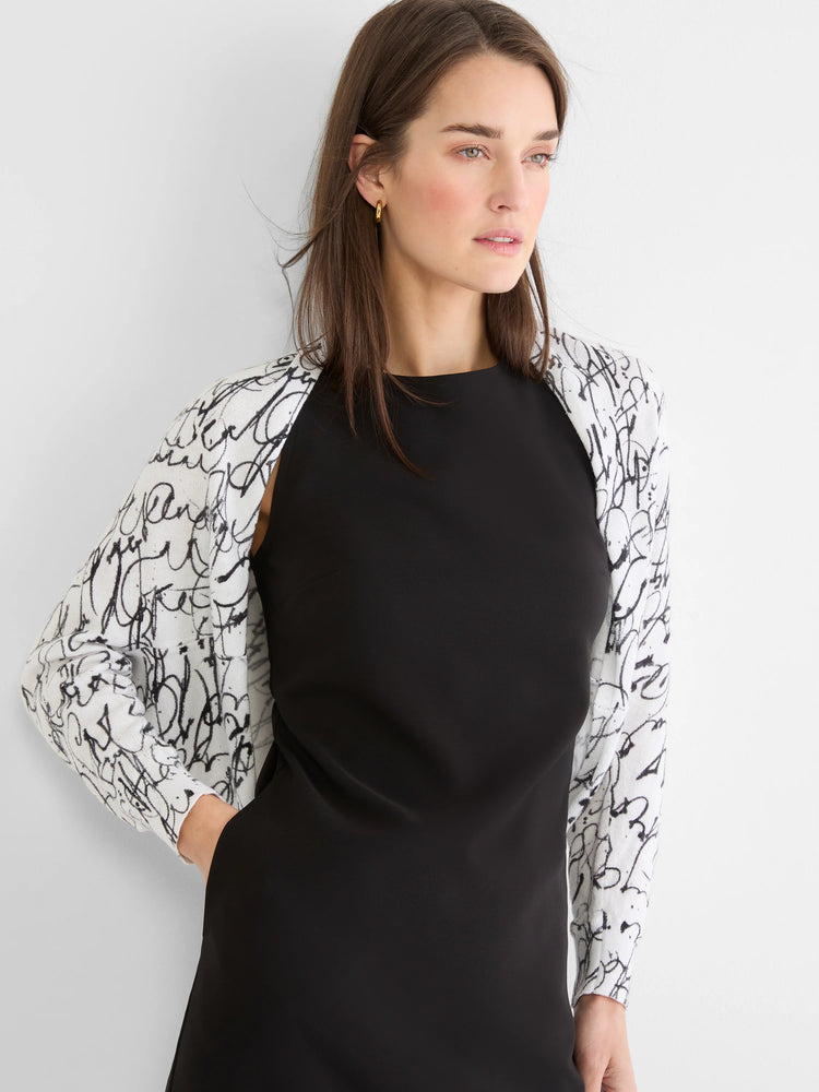 White knit shrug cardigan with black cursive pattern, worn open.