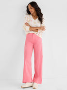 Model wears a cream patterned V-neck sweater and fitted high-waisted, wide-leg trousers in solid coral pink.