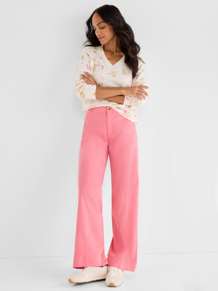 Model wears a cream patterned V-neck sweater and fitted high-waisted, wide-leg trousers in solid coral pink.