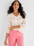 She wears a relaxed V-neck sweater in ivory featuring an abstract pattern of pink and beige blocks.