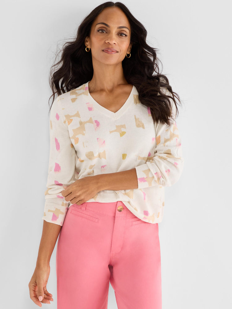 She wears a relaxed V-neck sweater in ivory featuring an abstract pattern of pink and beige blocks.