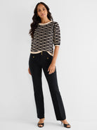 A black and tan striped knit sweater with 3/4 sleeves is paired with fitted black trousers detailed with gold nautical.