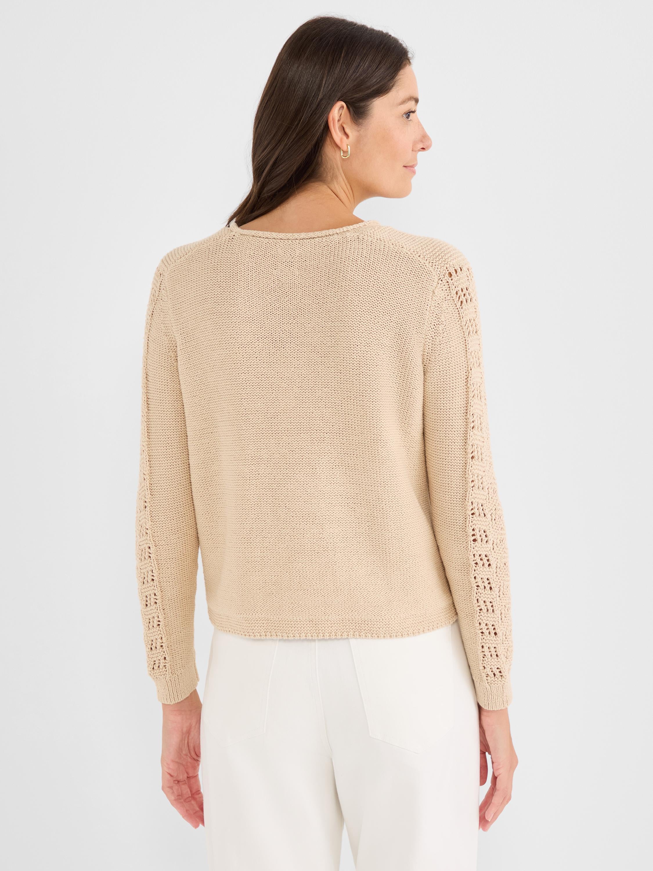 Model wears a relaxed fit beige knit sweater featuring a crew neck and eyelet stitch details along the long sleeves.