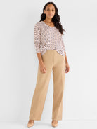 Model wears a fitted pink patterned V-neck top tucked into wide-leg, high-waisted camel trousers.