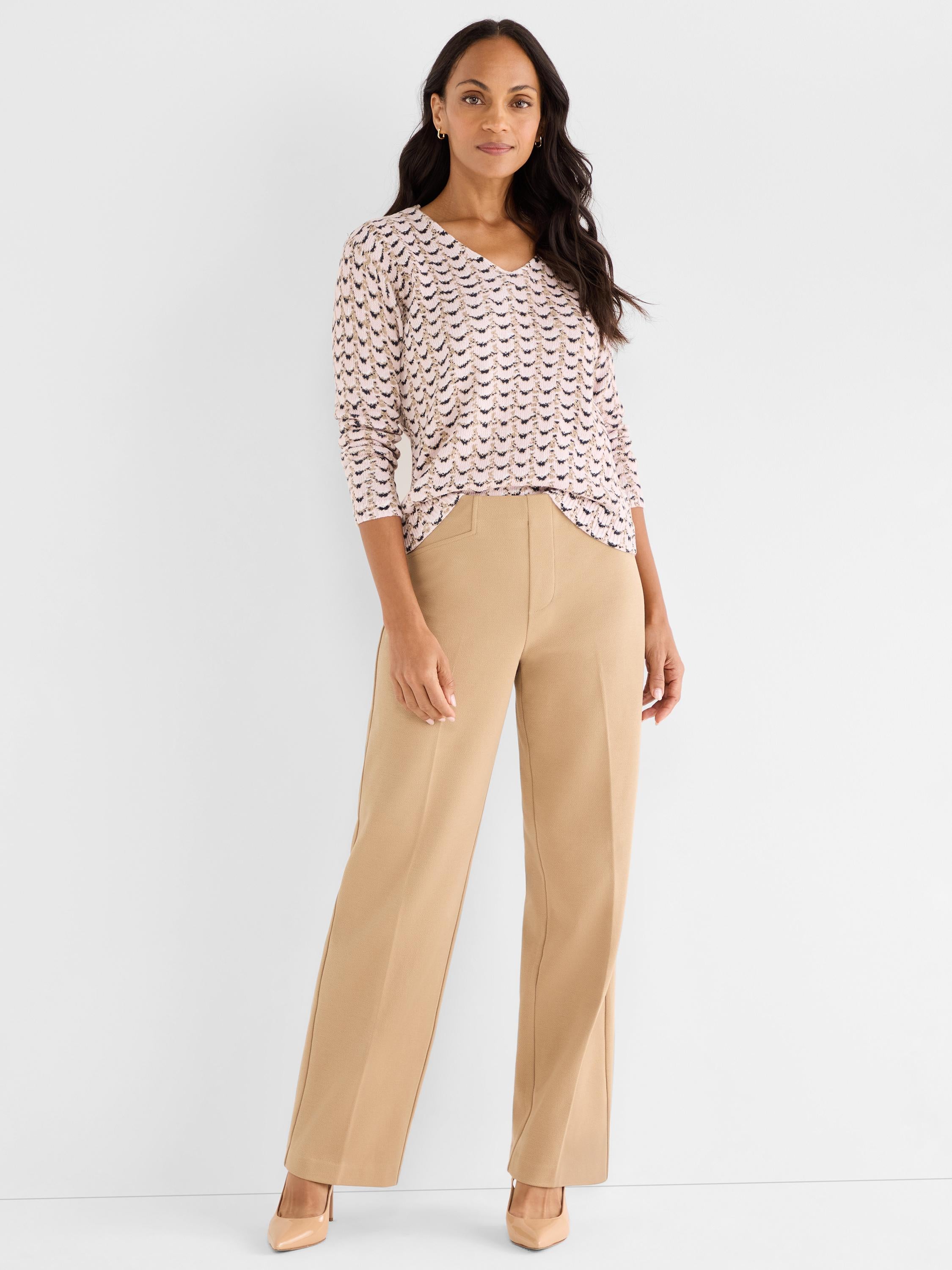 Model wears a fitted pink patterned V-neck top tucked into wide-leg, high-waisted camel trousers.