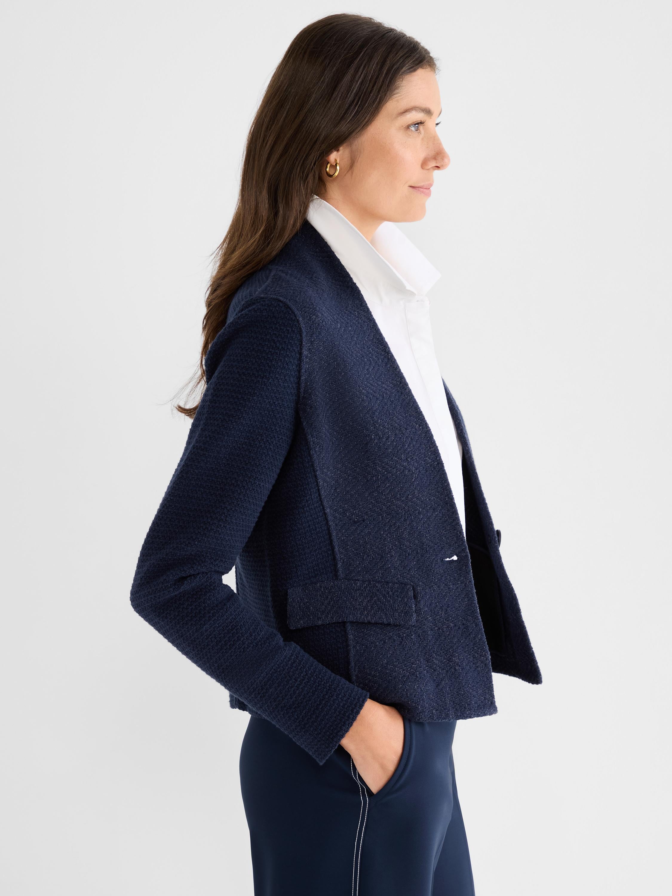 The model wears a fitted navy textured knit cropped blazer with an open front and patch pockets over a white shirt.