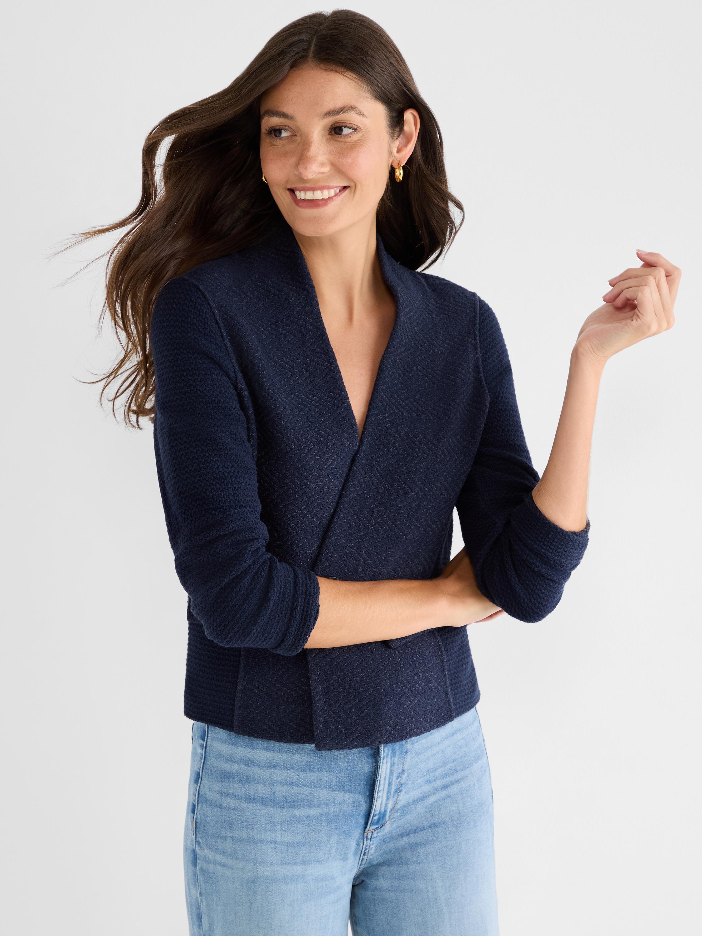 She models a fitted, cropped navy tweed jacket with a clean shawl lapel over light wash jeans.