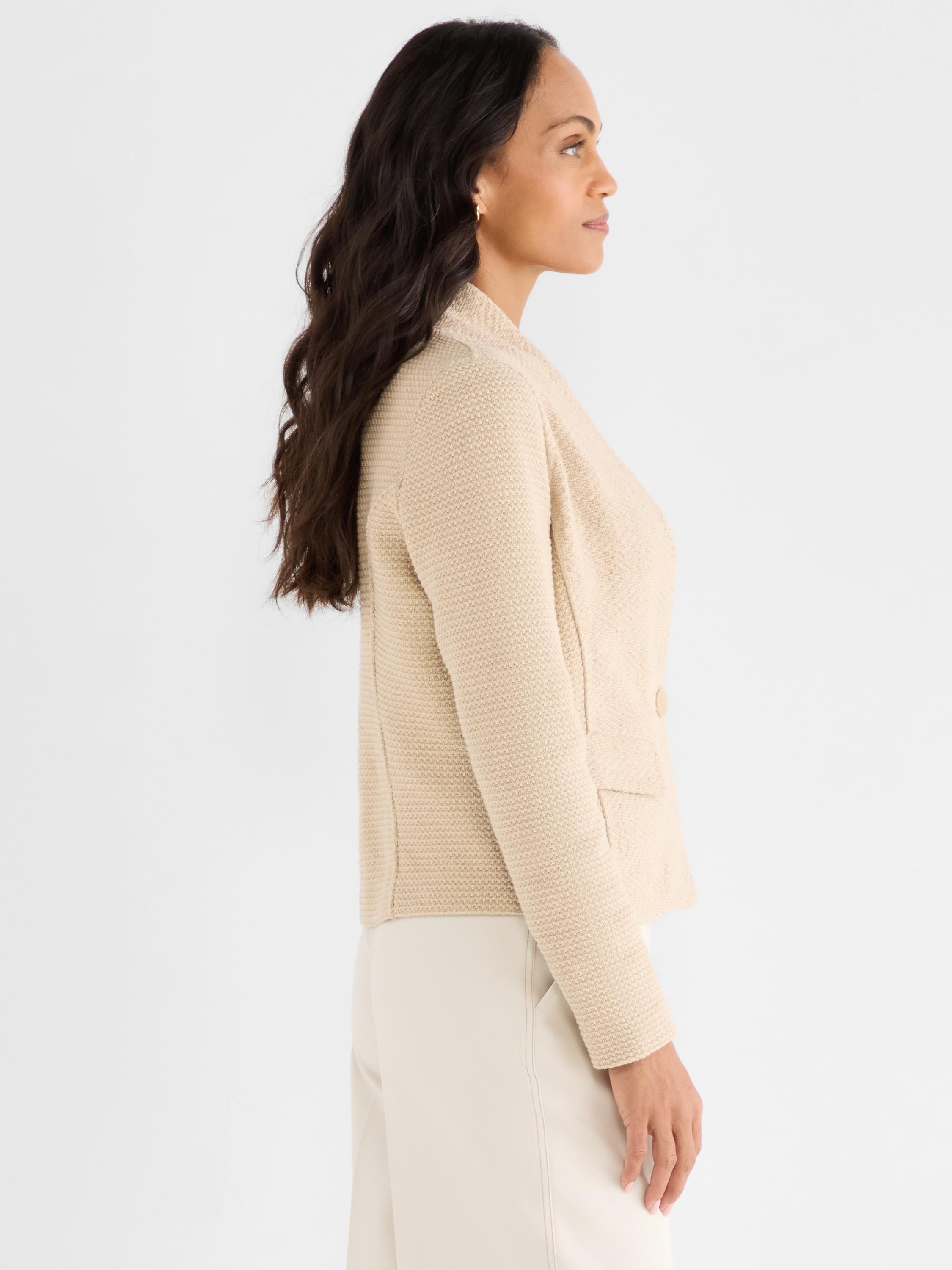 Model wears a fitted beige knit blazer with a textured stitch and a single-button closure.