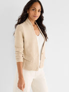 Model wears a tailored, light beige knit jacket featuring a textured finish, cropped length, and collarless open front.