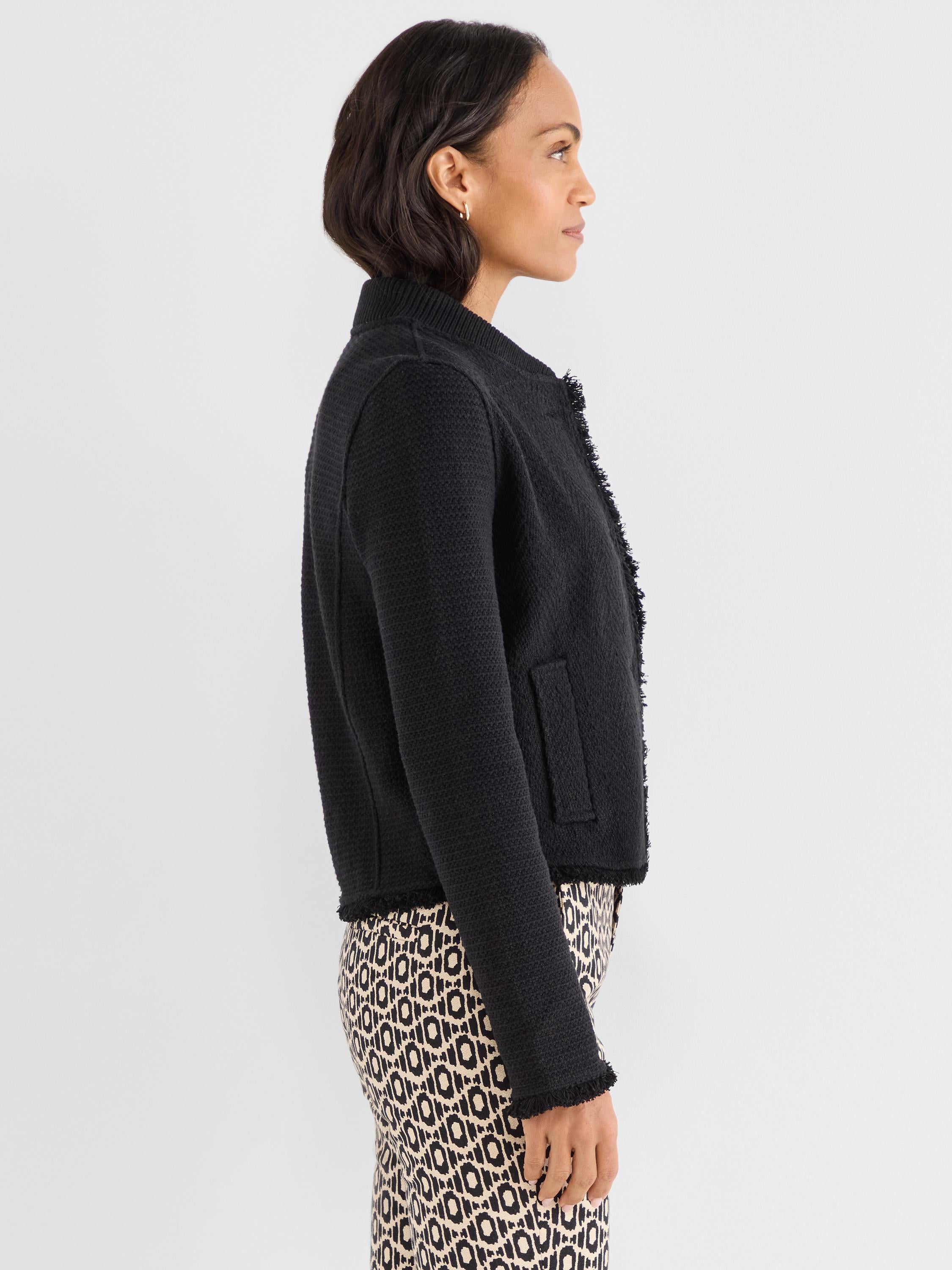 Black tailored knit jacket with a cropped hem, collarless neckline, and pronounced fringe trim detailing.