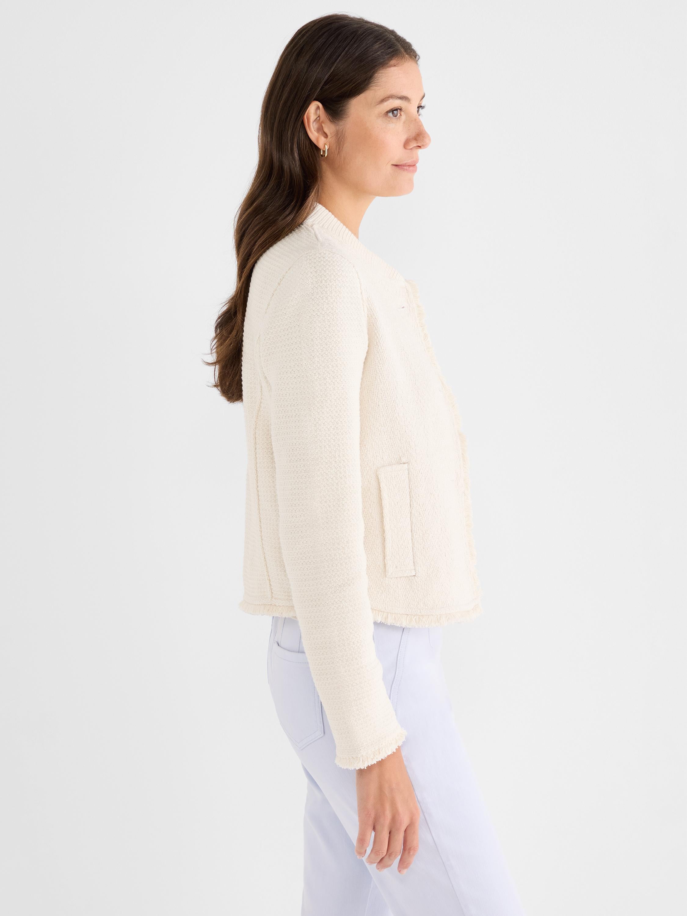 A fitted cream knit jacket features a collarless neckline, patch pockets, and frayed edge trim.