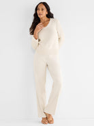 A model wears a cropped ivory ribbed V-neck sweater with crochet trim and fitted wide-leg beige trousers.