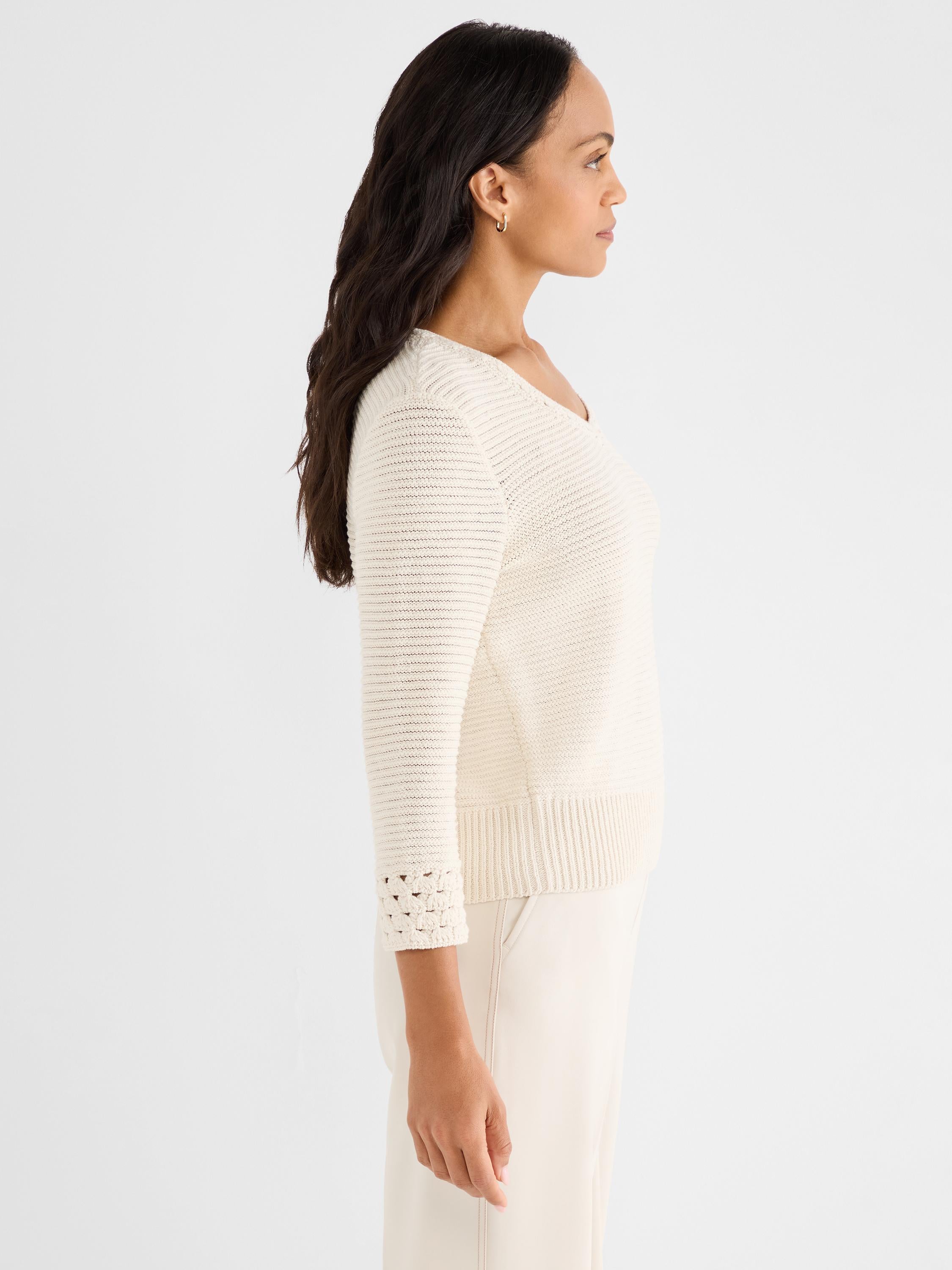 The model wears a fitted cream textured-knit sweater with a scoop neck and patterned three-quarter cuffs.