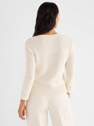 Fitted cream knit sweater features subtle textured stitching, a ribbed hem, and open crochet cuffs.