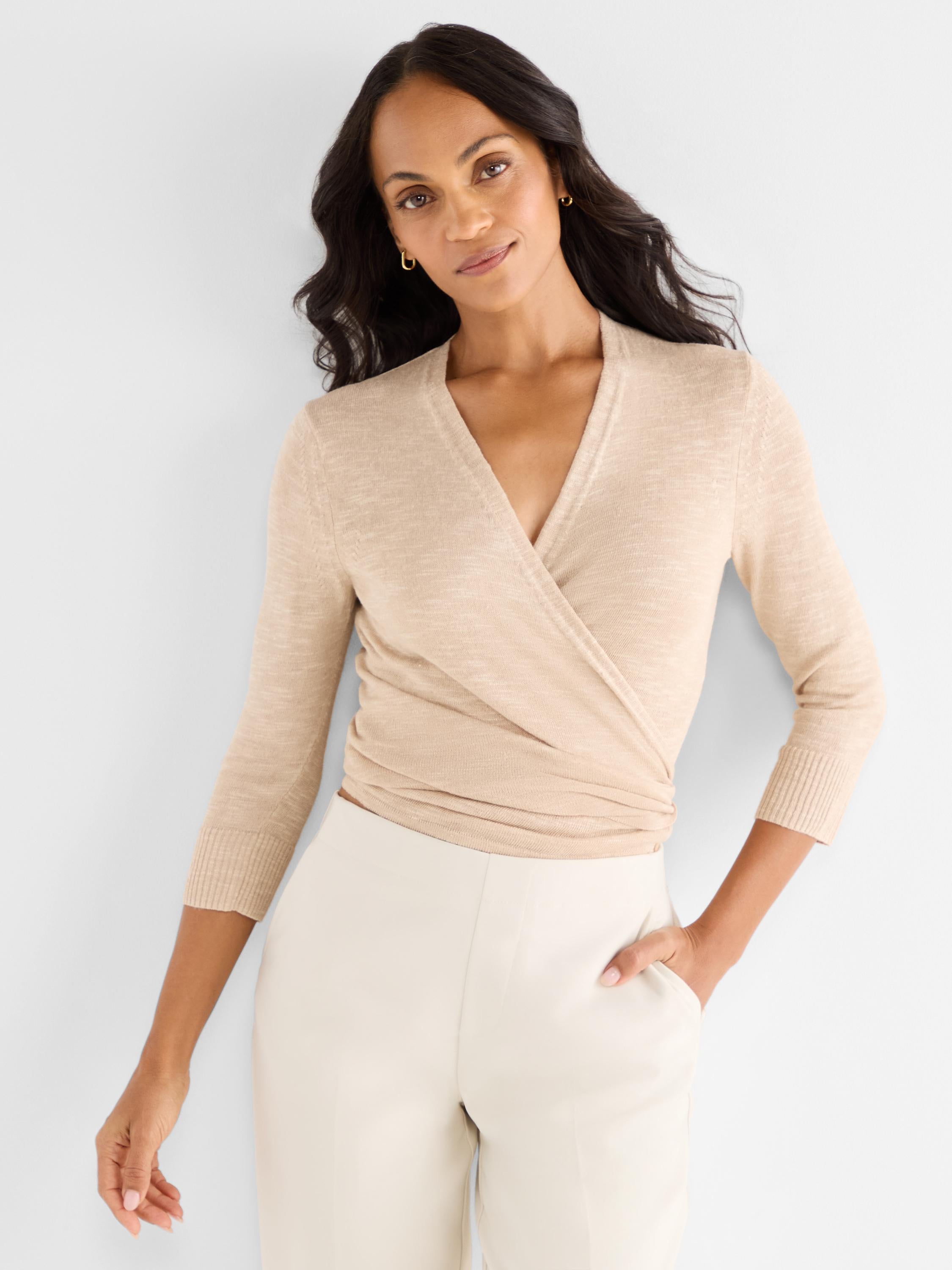 A model wears a fitted light tan knit wrap top with a deep V-neck and three-quarter sleeves.