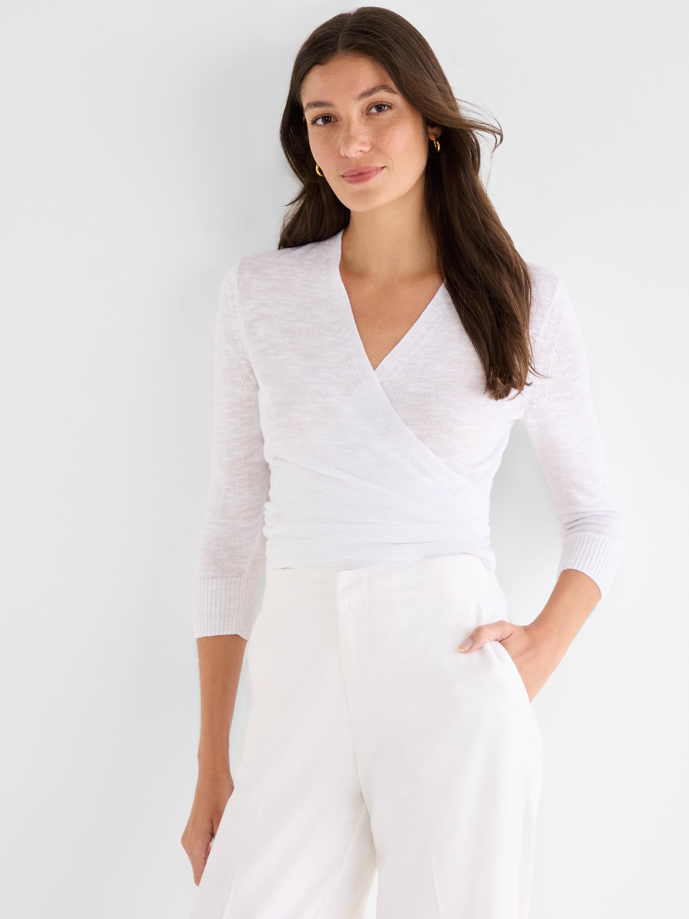 Fitted white sheer knit ballet wrap top featuring a V-neckline and three-quarter sleeves, paired with white trousers.