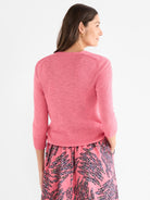 The model wears a fitted pink crewneck sweater with a fine marled knit texture and three-quarter length sleeves.