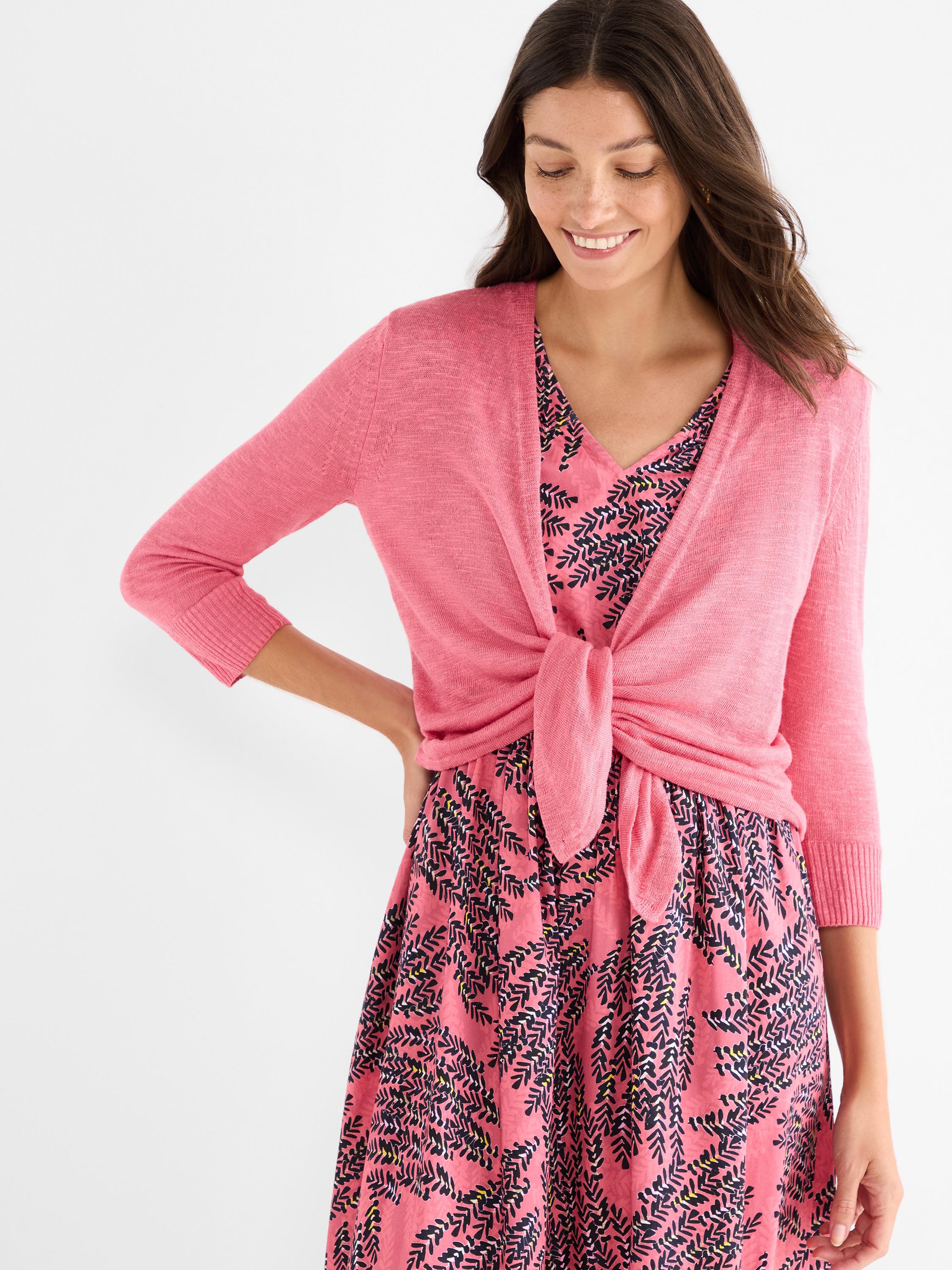 Bright pink lightweight cardigan featuring three-quarter sleeves and a front tie detail is styled over a printed dress.