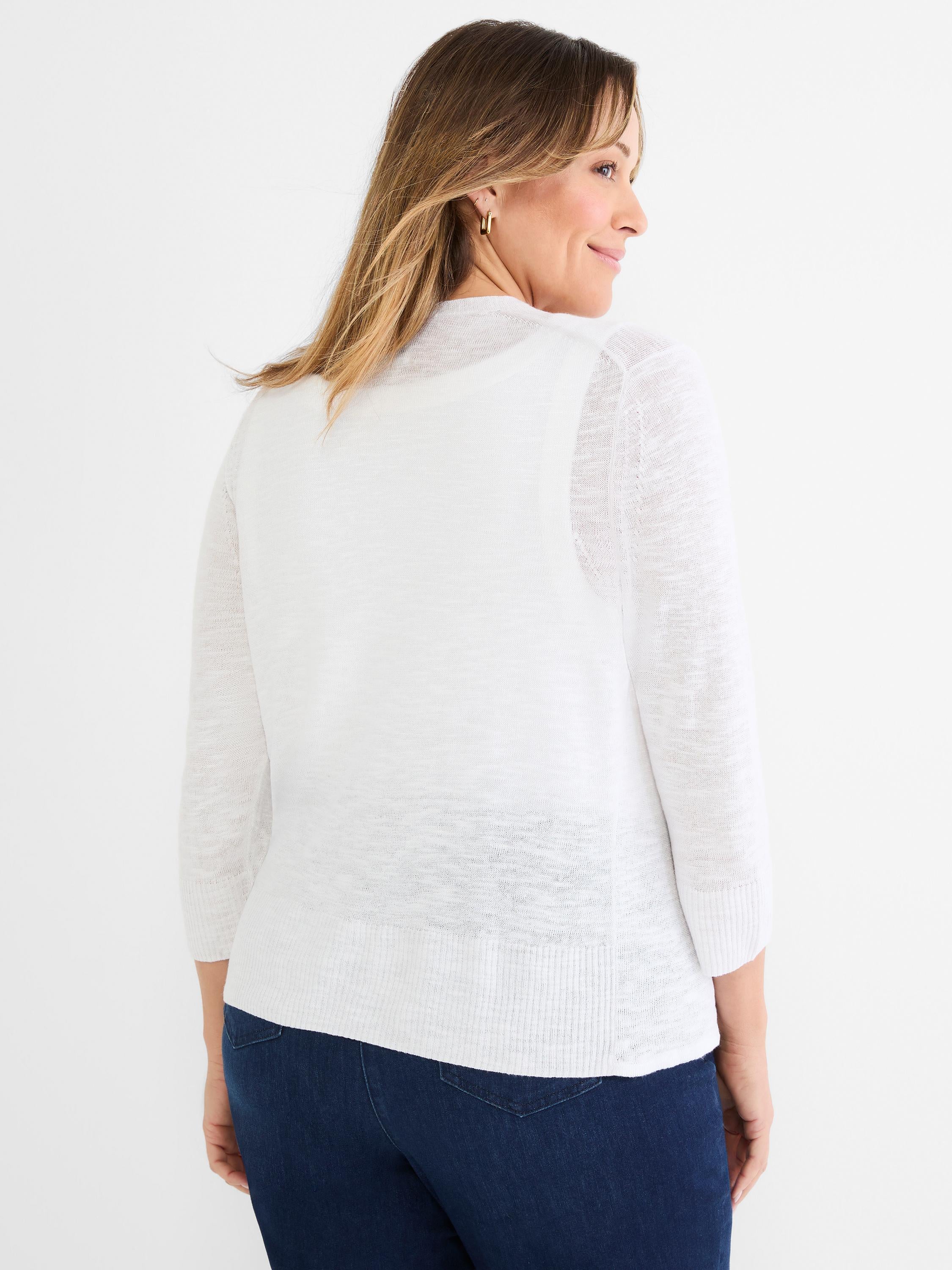 She wears a relaxed fit white knit cardigan with 3/4 length sleeves and a ribbed hem over dark jeans.
