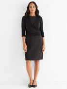 Black knit wrap sweater with 3/4 sleeves styled over a fitted knee-length black dress.