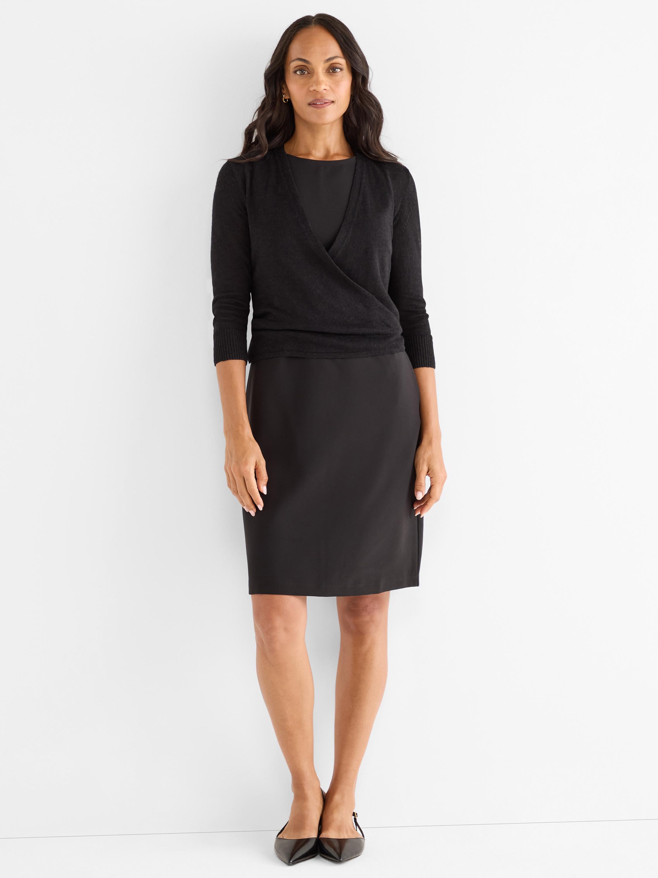 Black knit wrap sweater with 3/4 sleeves styled over a fitted knee-length black dress.