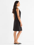 A model wears a classic, tailored black sleeveless sheath dress featuring a clean design and hitting above the knee.