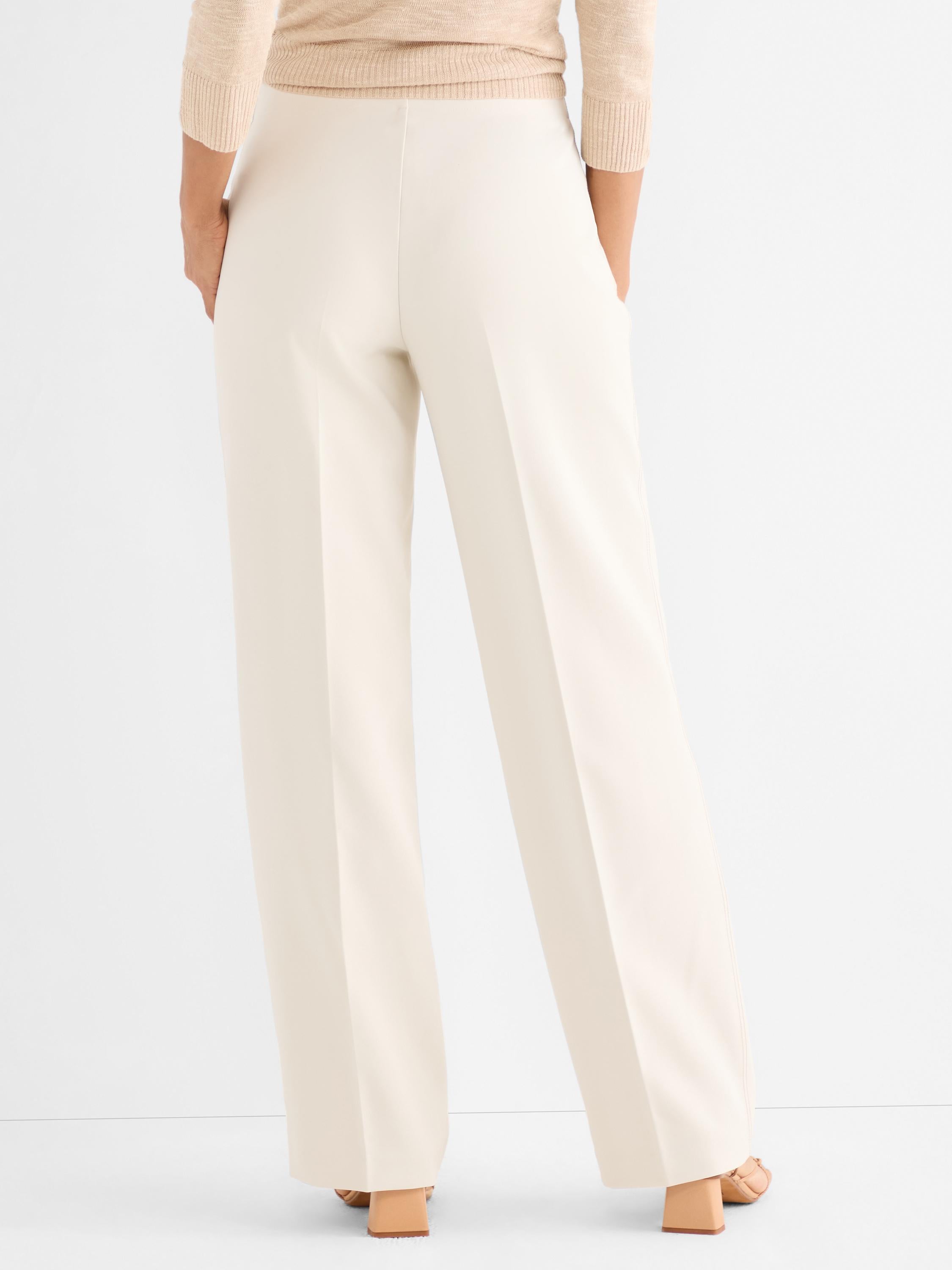 Elegant cream wide-leg trousers are styled high-waisted, showcasing a long, fluid drape and sharp pressed creases.