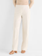 Model wears high-waisted tailored cream trousers with a straight leg and prominent front seams.