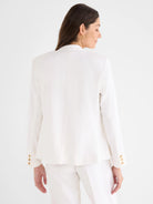 Back view of an off-white, collarless linen blazer. It features three tan buttons on each sleeve cuff.