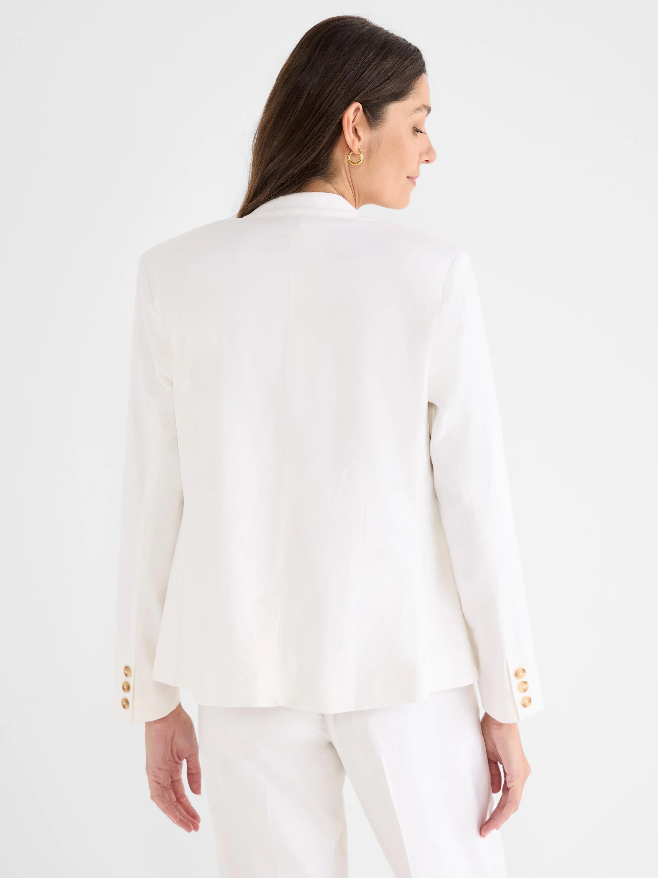 Back view of an off-white, collarless linen blazer. It features three tan buttons on each sleeve cuff.
