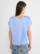 Light blue woven tee with a subtle sheen, relaxed fit, scoop neck, and short cap sleeves, shown from the back.