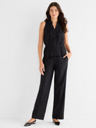 Black collared sleeveless top with a cinched waist and peplum is styled with wide-leg trousers.
