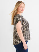 Black and beige patterned short-sleeve top featuring a loose fit and a scoop neck, paired with dark wash jeans.