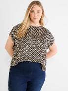 A boxy black and tan abstract print blouse with short sleeves is worn by the model with dark navy denim.