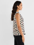 The model wears a relaxed fit sleeveless blouse featuring a black, white, and multicolored abstract geometric print.