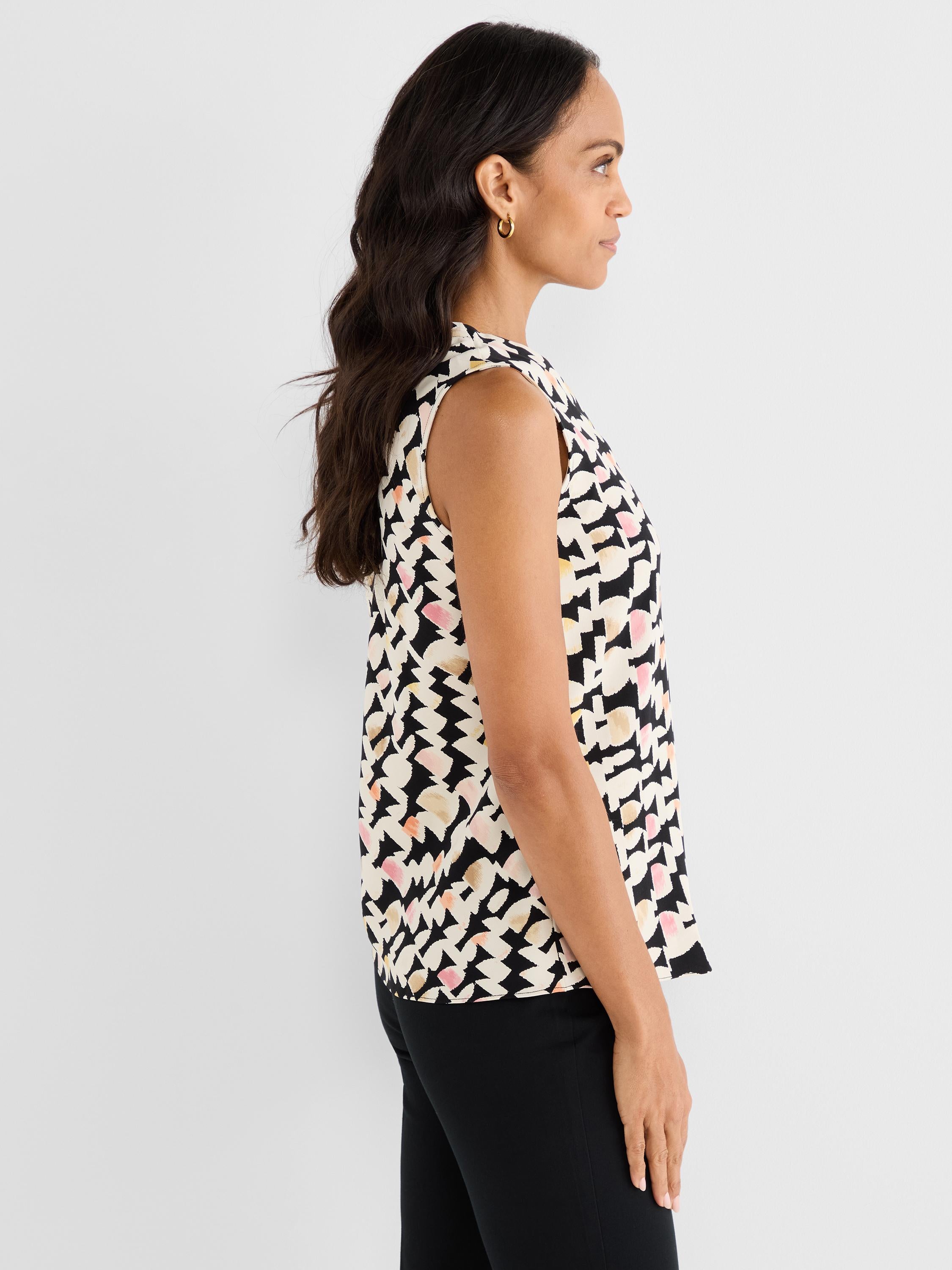 The model wears a relaxed fit sleeveless blouse featuring a black, white, and multicolored abstract geometric print.