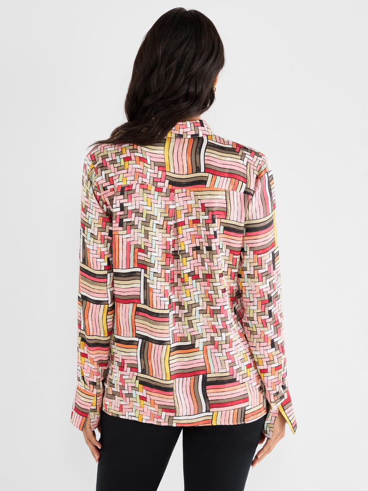 Model wears a relaxed long-sleeve blouse in a vibrant pink and multicolor geometric patchwork print with cuff slits.
