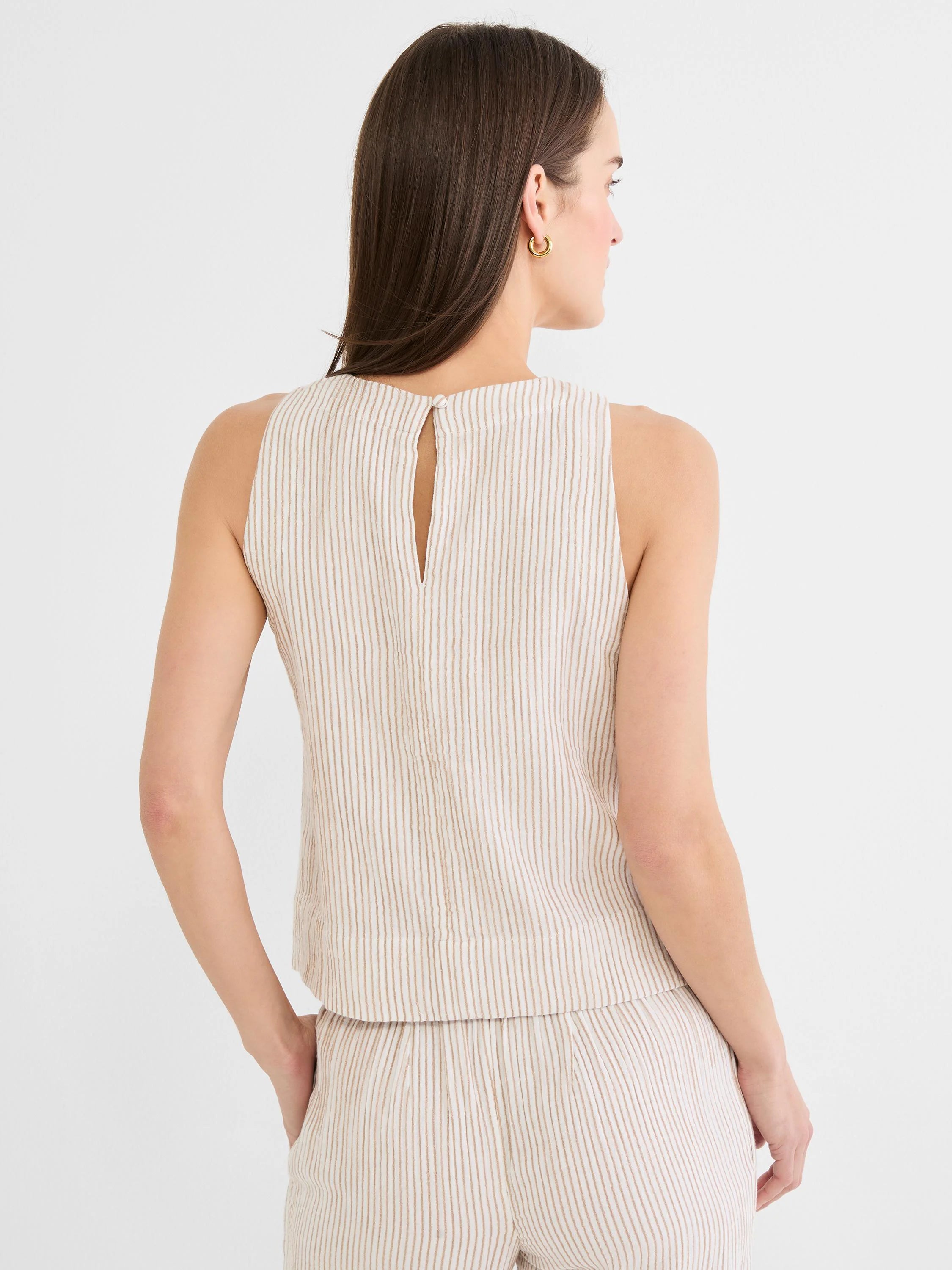 Back view of a cream sleeveless tank top with vertical brown pinstripes. Features a keyhole opening and button closure at...