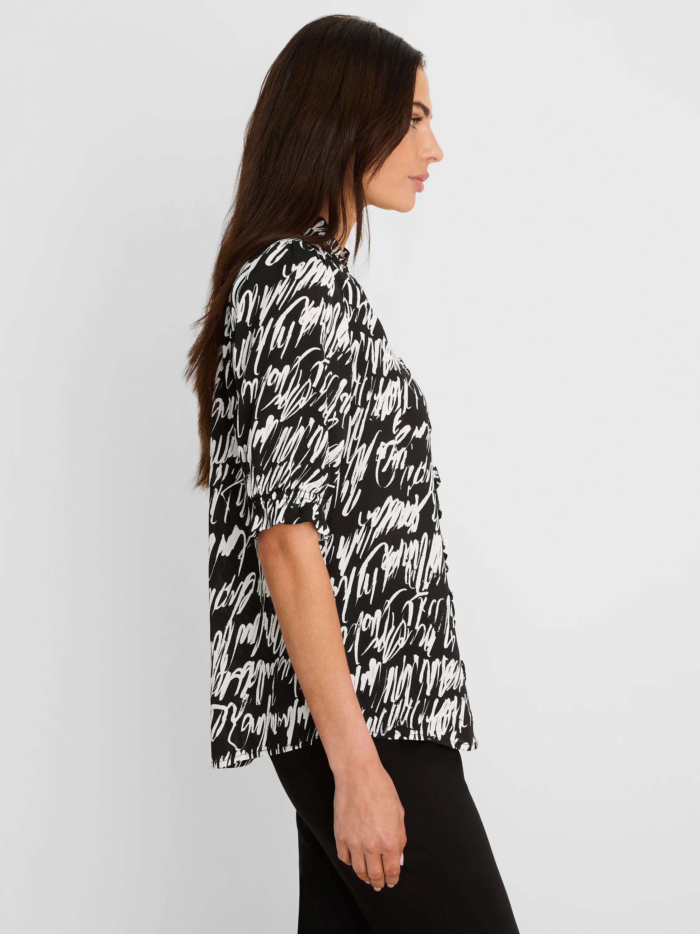 Black and white cursive print top with puffed short sleeves and a ruffled neckline, shown in profile.