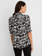 Black and white top with abstract cursive pattern, high ruffled neck, and gathered short sleeves.