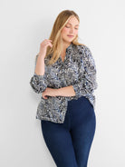 White shirt with jagged black and blue abstract lines. Features a collar and long sleeves. Worn by a model.