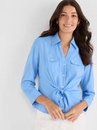 Light blue collared shirt with a front tie knot, long sleeves, and two white-buttoned chest pockets.