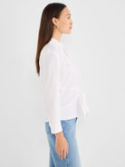 White collared tie-front shirt with long sleeves and a chest pocket, styled with light blue jeans.
