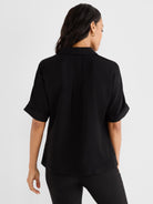 Black relaxed short-sleeved collared blouse features back pleating and folded cuffs.