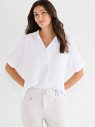 White relaxed-fit short-sleeve collared blouse worn by a model, featuring a deep V-neck and cuffed sleeves.