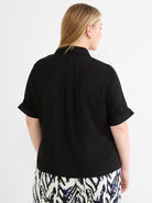 Flowy black collared blouse featuring short cuffed sleeves and a subtle back pleat detail.