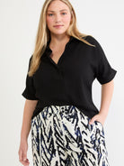 Black relaxed short sleeve shirt featuring an open collar and cuffed sleeves, shown over high-waisted abstract patterned.