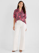 A relaxed pink and black patterned blouse with a ruffled neck is styled with high-waisted wide white pants.